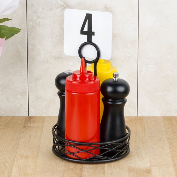 A black American Metalcraft birdnest condiment caddy with a red card holder holding a black pepper mill and a red container.