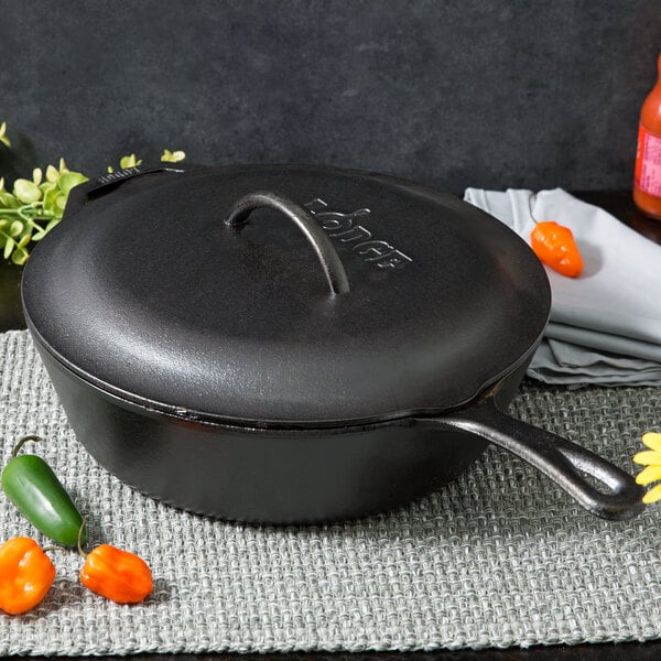 A Lodge cast iron deep skillet with a lid on a table with peppers.