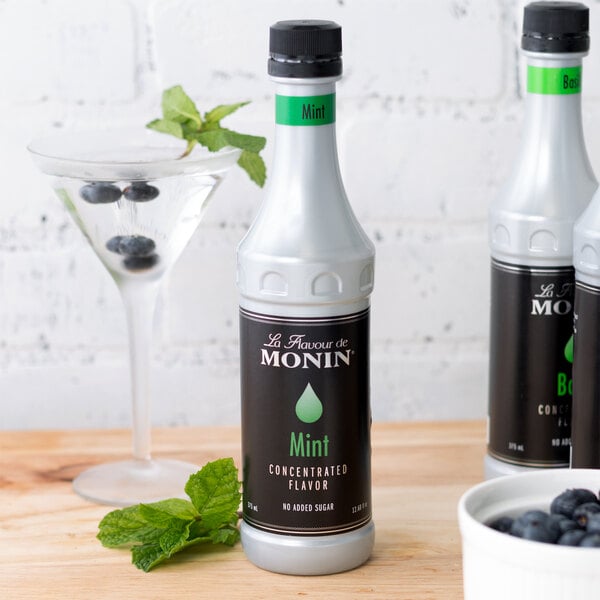 A close-up of a white Monin Mint Concentrated Flavor bottle with a black label.