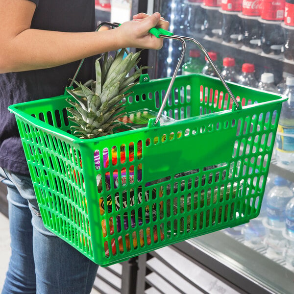 A person holding a Regency Green plastic shopping basket with food in it.