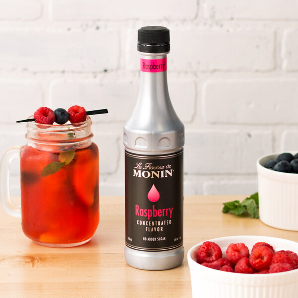 A bottle of Monin Raspberry Concentrated Flavor next to a bowl of raspberries.