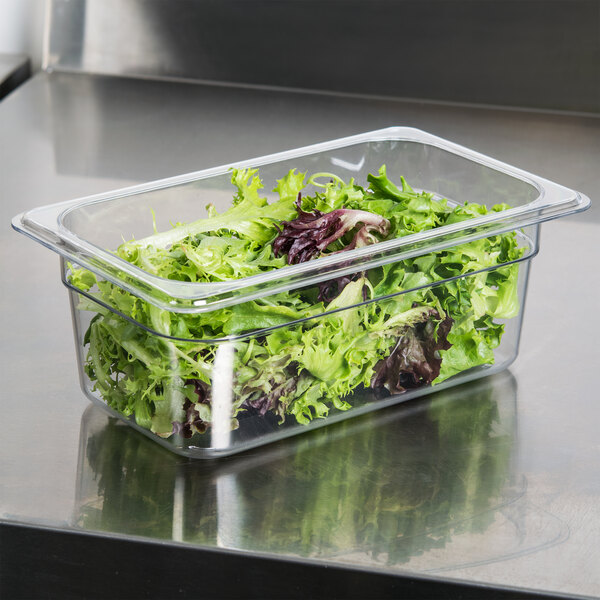 A Carlisle clear plastic food pan filled with lettuce on a counter.