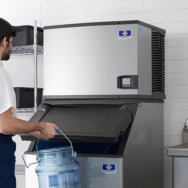 A man in a white cap holding a bucket of water standing next to a Manitowoc water cooled ice machine.