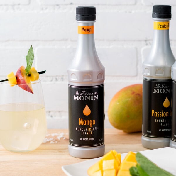 A close up of a bottle of Monin Mango Concentrated Flavor next to a glass of liquid.