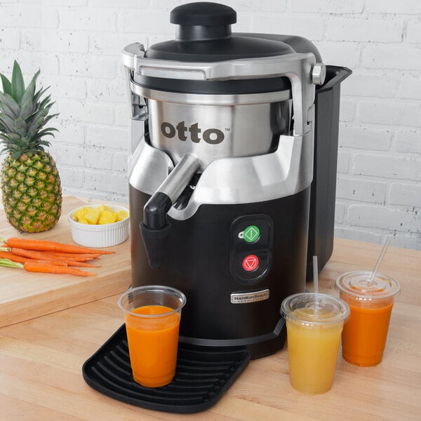 A Hamilton Beach Otto Auto Feed Juice Extractor with cups of juice and a glass of orange juice.