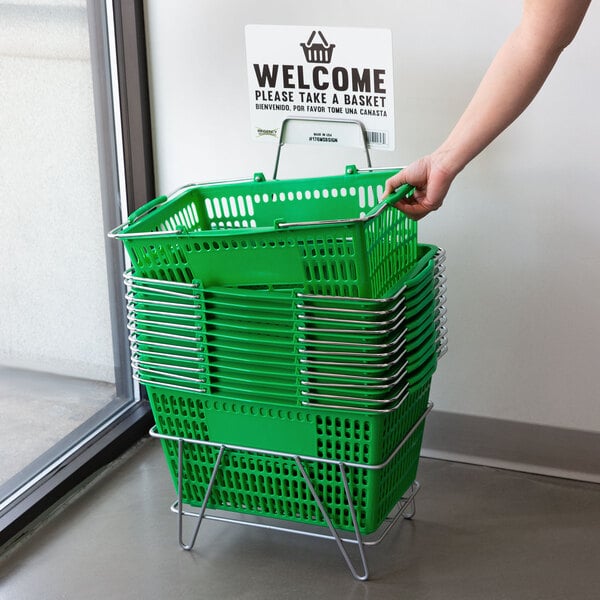 A person holding a green Regency shopping basket with a sign.