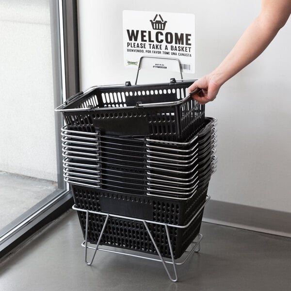 A person holding a Regency black plastic grocery market shopping basket with a welcome sign.