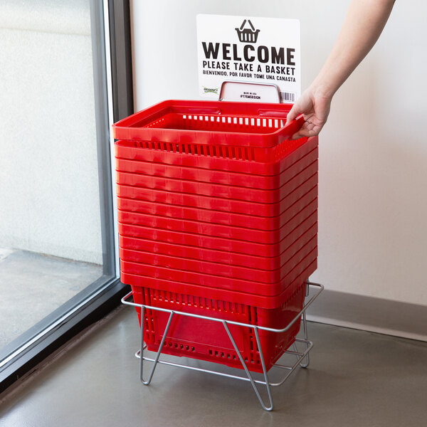 A hand holding a Regency Red plastic shopping basket with a sign stand.
