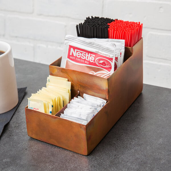 An American Metalcraft copper bar caddy on a hotel buffet counter with sugar packets and straws inside.