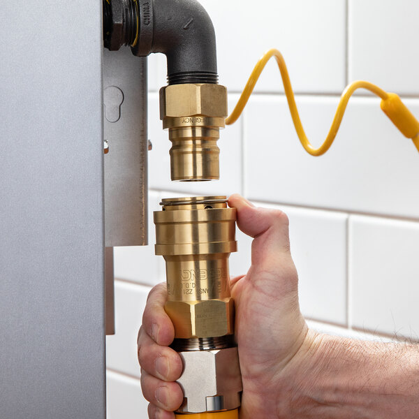 A hand using a Regency quick disconnect fitting to connect a yellow hose to a metal pipe.