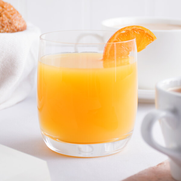A glass of Tropicana orange juice with a slice of orange on top of it.