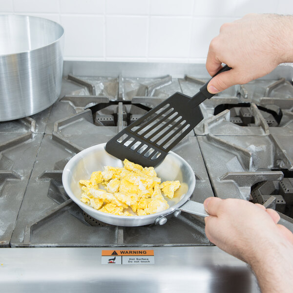 A person using a Vollrath Arkadia aluminum fry pan to cook scrambled eggs.