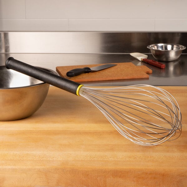 A Matfer Bourgeat stainless steel whisk with a red Exoglass handle in a bowl on a counter.