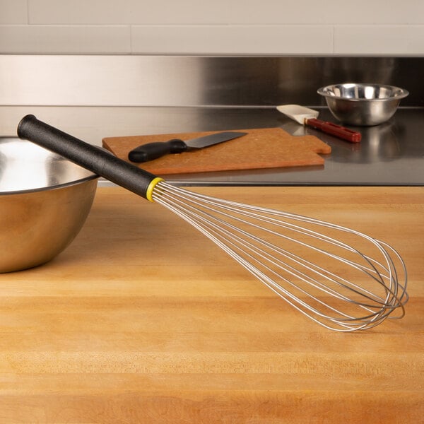A Matfer Bourgeat stainless steel whisk with an Exoglass handle sitting on a wooden counter next to a bowl.
