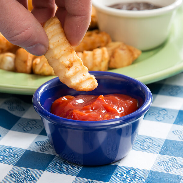 A hand holding a french fry being dipped into a navy blue Thunder Group melamine ramekin.