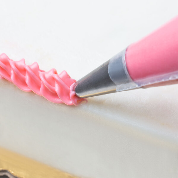 A hand using an Ateco Cross-Top Piping Tip to decorate a cake with pink frosting.