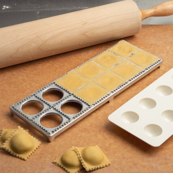 A metal tray with ravioli and a rolling pin on a table.
