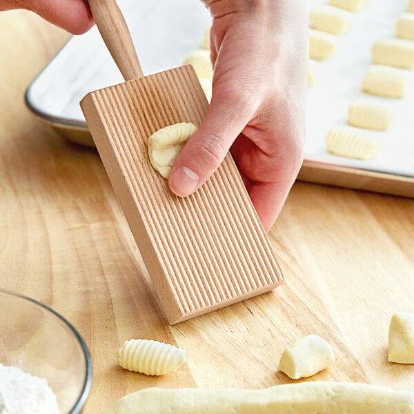 A person using a Fox Run beech wood gnocchi board to make gnocchi on a wooden surface.