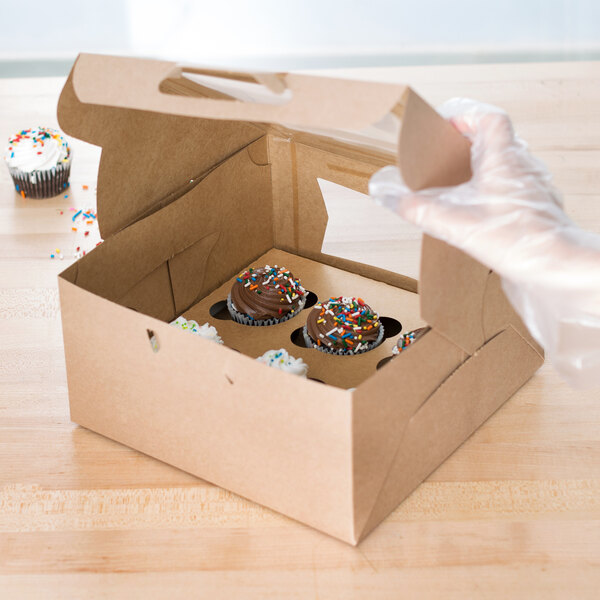 A hand holding a Baker's Mark kraft cupcake box with a frosted cupcake inside.