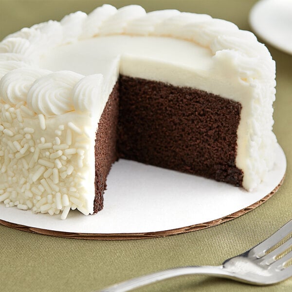 A slice of white-frosted cake on a white corrugated cake circle with a silver spoon.