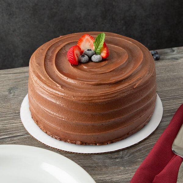 A 10" corrugated white cake circle with a chocolate cake topped with strawberries and blueberries on a table in a bakery display.