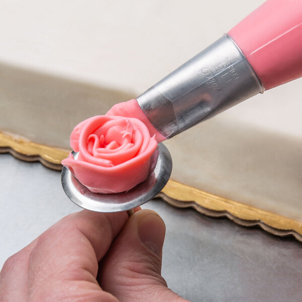 A person using an Ateco 118 rose piping tip to decorate a pink rose on a cake.