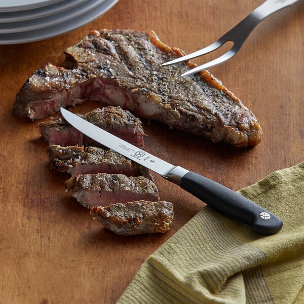 A steak with a Mercer Culinary Genesis® steak knife on a cutting board.