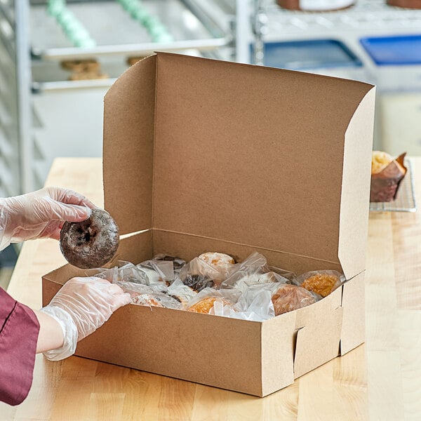 A person wearing gloves puts a donut in a Kraft bakery box.