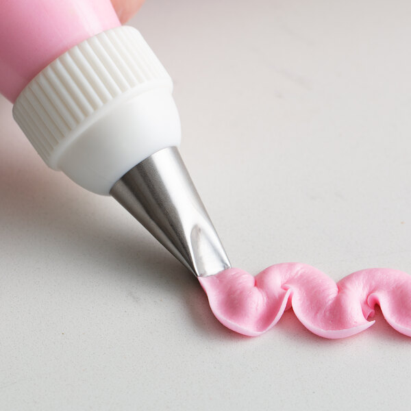 A person using a pink plastic pastry bag with an Ateco curved petal piping tip to make a pink ribbon.