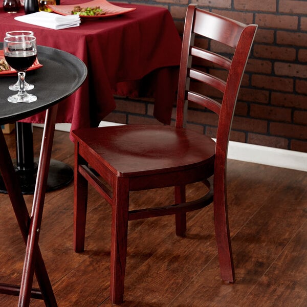 A Lancaster Table & Seating mahogany wood chair with a mahogany wood seat next to a table with a glass of wine.