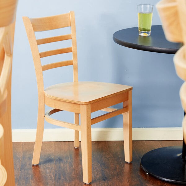 A Lancaster Table & Seating wooden ladder back chair with a natural wood seat next to a table.