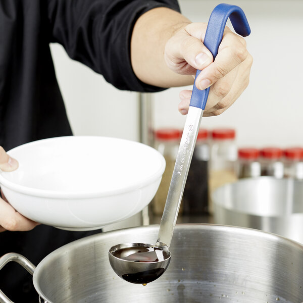 A person using a Vollrath Jacob's Pride stainless steel ladle with a blue Kool-Touch handle to pour liquid into a bowl.