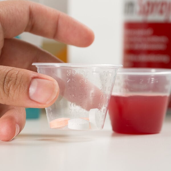 A hand holding a Choice disposable polypropylene medicine cup with pills in it.