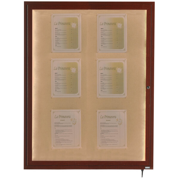 A white Aarco walnut finish bulletin board cabinet with several papers on it.
