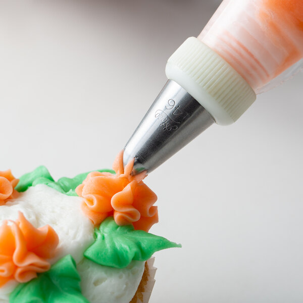 A person using an Ateco drop flower piping tip to pipe icing on a cupcake.