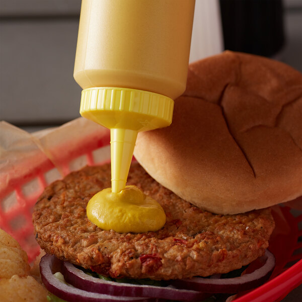 A close-up of a mustard bottle on top of a burger bun.