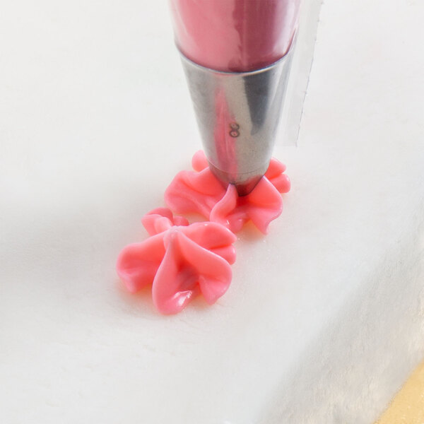 A pink Ateco drop flower piping tip being used with a pastry bag to pipe pink icing.