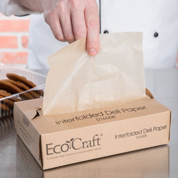 A hand holding a Bagcraft EcoCraft deli wrap.
