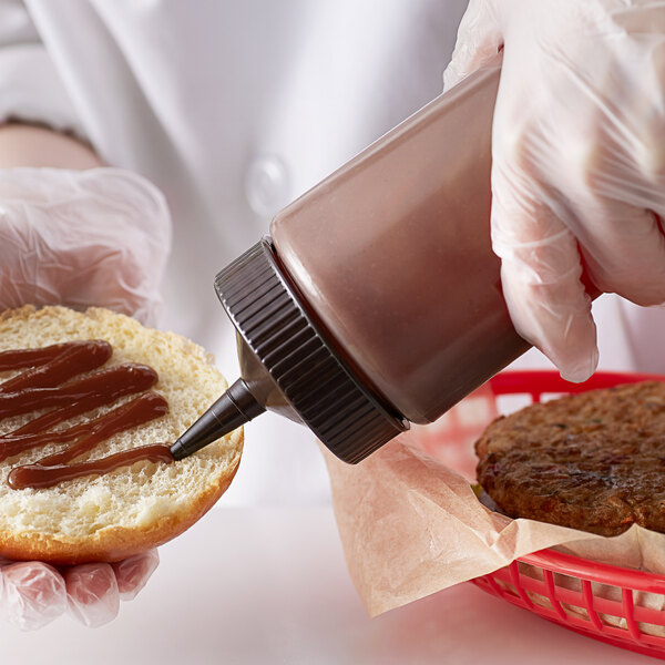 A hand using a Vollrath Clear Squeeze Bottle to put sauce on a burger bun.