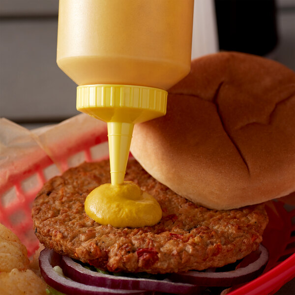 A burger with mustard being poured from a yellow Vollrath squeeze bottle.
