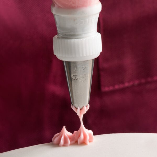 A pastry bag with a Ateco Drop Flower piping tip piping pink frosting onto a cake.
