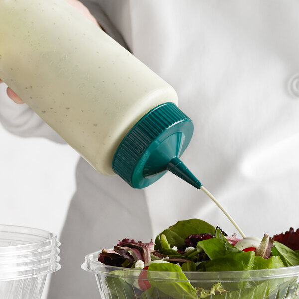A person using a Vollrath Clear Squeeze Bottle with a green tip to pour dressing onto a salad.
