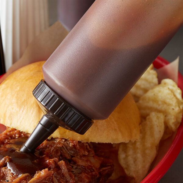 A person using a Vollrath Traex squeeze bottle to pour sauce on pulled pork.