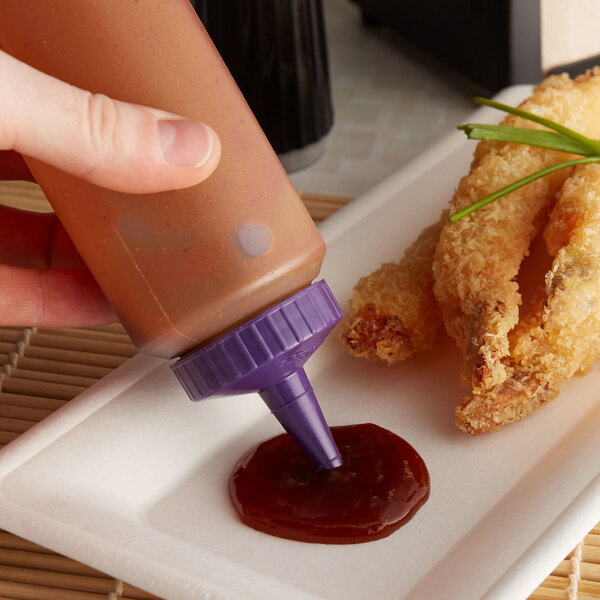 A hand holding a Vollrath Clear Squeeze Bottle with Purple Cap pouring sauce onto a plate of fried shrimp.