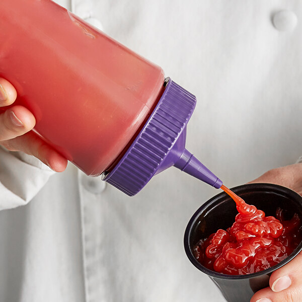 A person using a Vollrath Traex wide mouth squeeze bottle with purple cap to pour sauce into a cup of food.