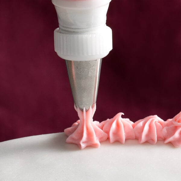 A cake being decorated with a white plastic Ateco closed star piping tip using a pastry bag.
