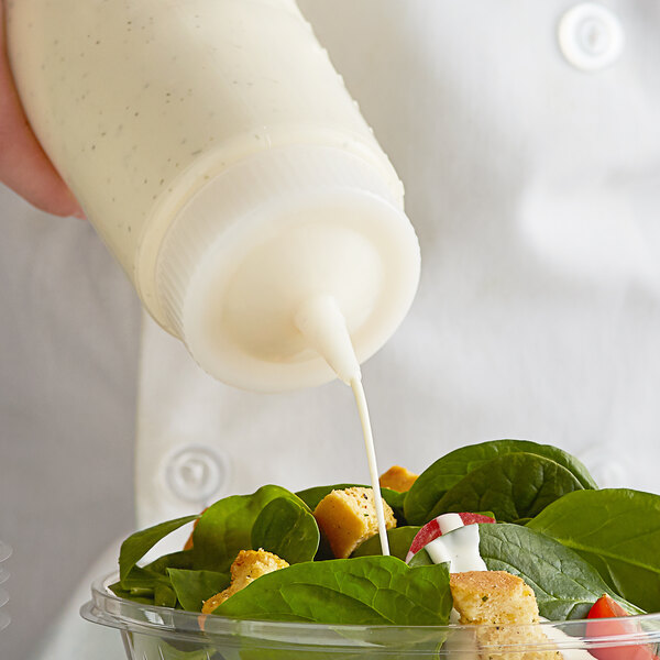 A hand using a Vollrath Color-Mate squeeze bottle to pour dressing onto a salad.