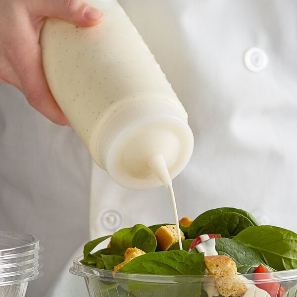 A person using a Vollrath clear squeeze bottle to pour dressing onto a salad.