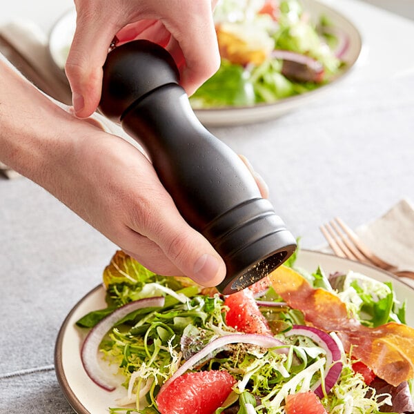 A person grinding Acopa Matte Black Wooden Salt / Pepper Mill over a plate of salad.