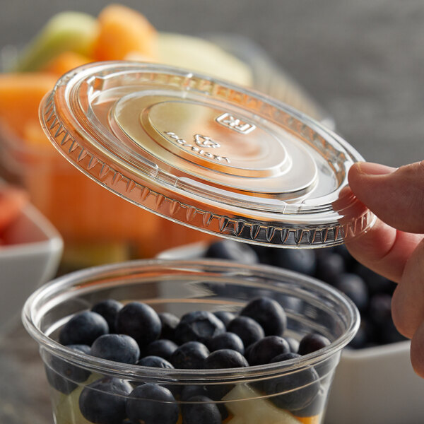 A hand using a Fabri-Kal clear plastic lid to cover a plastic cup of fruit.
